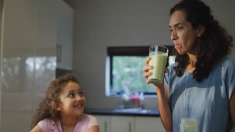 Mixed-race-mother-and-daughter-drinking-smoothie-in-the-kitchen