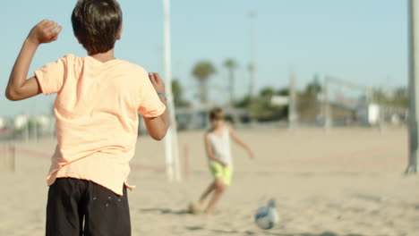 close-up shot of boy kicking ball to his friend on sandy shore