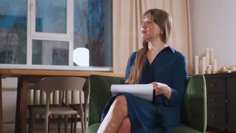 restorative practitioner speaking intentionally to female patient holding pen and notebook on lap in therapy room with window showing darkening sky, table with chairs beside and warm indoor lighting