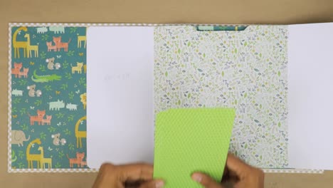 hands arranging pages in a colorful baby scrapbook album with cute animal designs and patterns