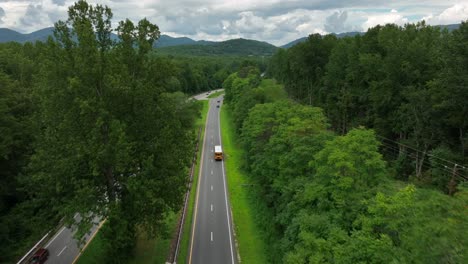 Aerial-tracking-yellow-school-bus-through-rural-mountains-in-USA