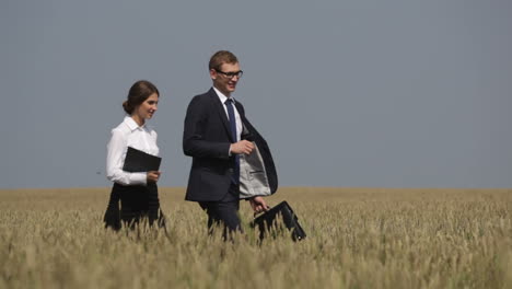 hombre de negocios y mujer de negocios caminando por un campo de trigo mientras habla a la luz del día