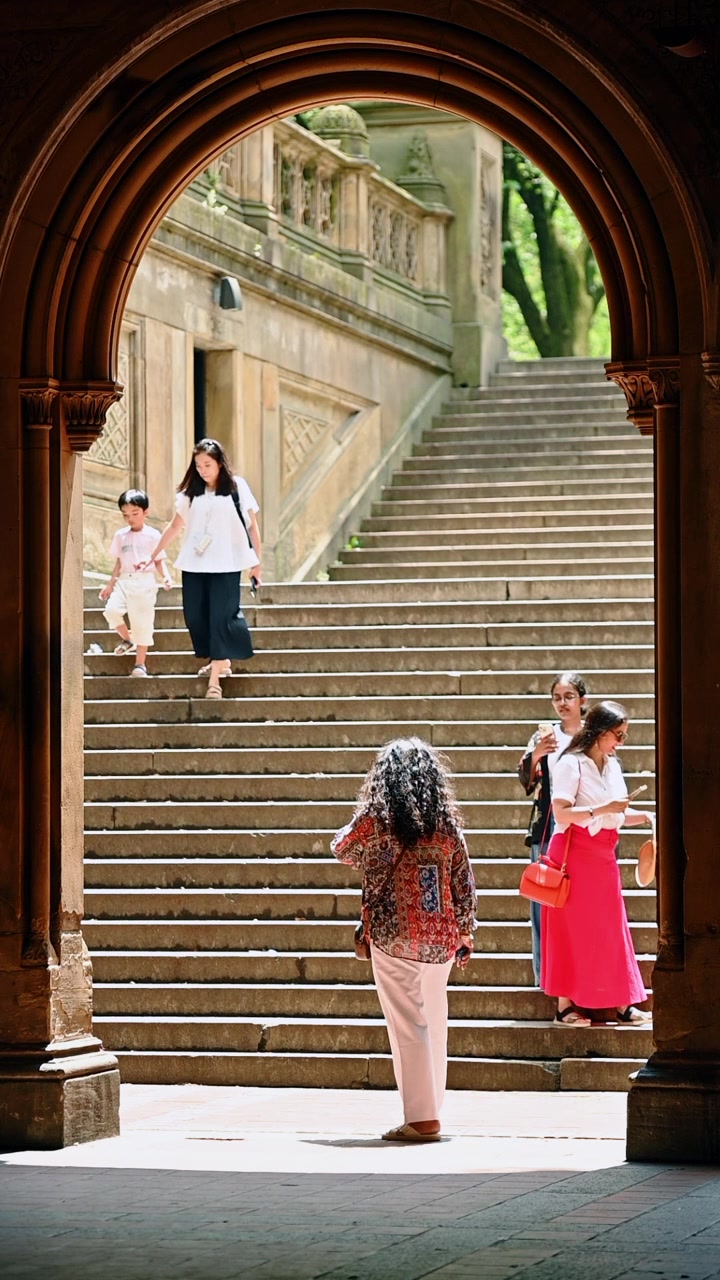 New York, USA, 22 maggio 2026: Visitatori sulla scalinata sotto l'arco di Bethesda Terrace, Central Park, New York. Arco in arenaria che incornicia figure su gradini illuminati dal sole con balaustra intagliata
