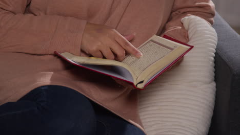 close up of muslim woman sitting on sofa at home reading or studying the quran 4