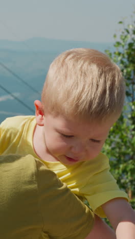 loving mother embraces little boy enjoying view of highland with poma lift against old distant mountains at bright sunlight closeup slow motion