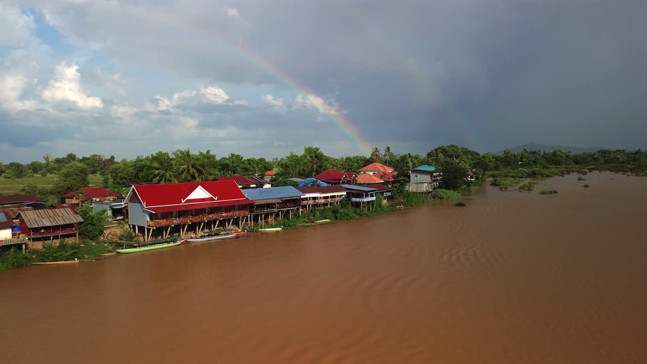 Barche e case su palafitte lungo un fiume calmo a Don Det in Laos con una calda atmosfera tropicale diurna, vista aerea