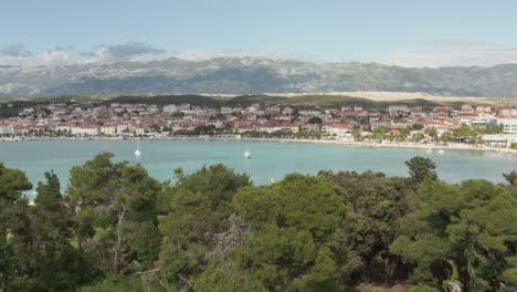 Luftaufnahme:-Flug-über-Bäume,-Um-Einen-Wunderschönen-Türkisblauen-Ozean-Zu-Enthüllen,-Land-In-Novalja,-Kroatien-Natur-Mit-Häusern-Und-Blauem-Himmel-Und-Sonne