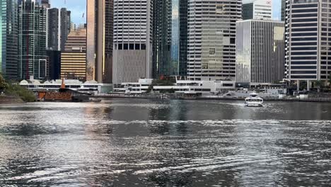 Public-transportation-river-ride,-citycats-ferry-cruising-from-business-central-district-riverside-terminal-during-the-day-with-shimmering-river-water-reflection