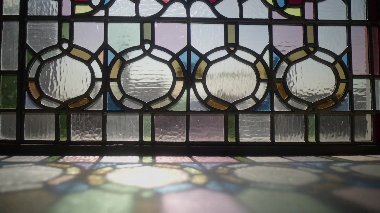 Panning camera showing stained-glass window at home, showing detail as sun casting color on sill