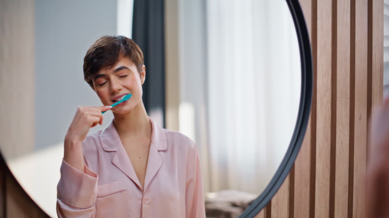 Closeup satisfied girl tooth brushing morning time indoors. Woman looking mirror