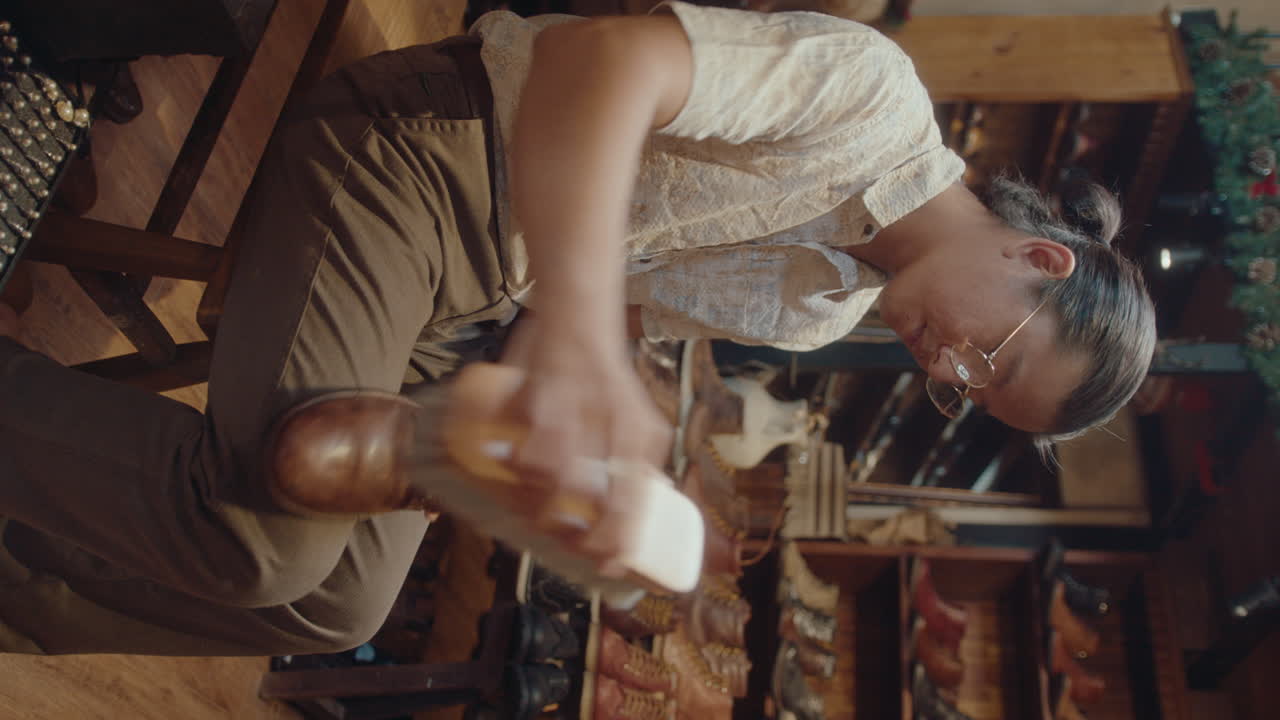Asian Man Working with Old Leather Boots in Restoration Workshop