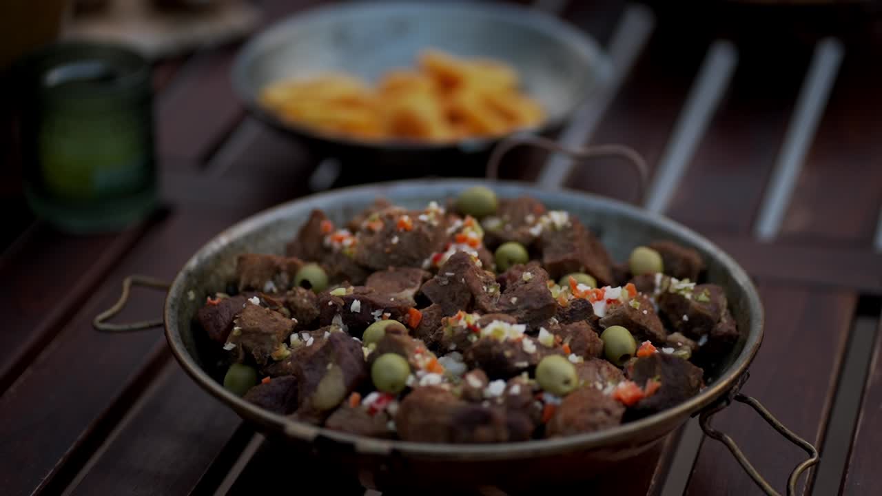chunks of stewed meat with green olives and vegetables served in a rustic pan outdoors
