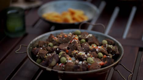 chunks of stewed meat with green olives and vegetables served in a rustic pan outdoors