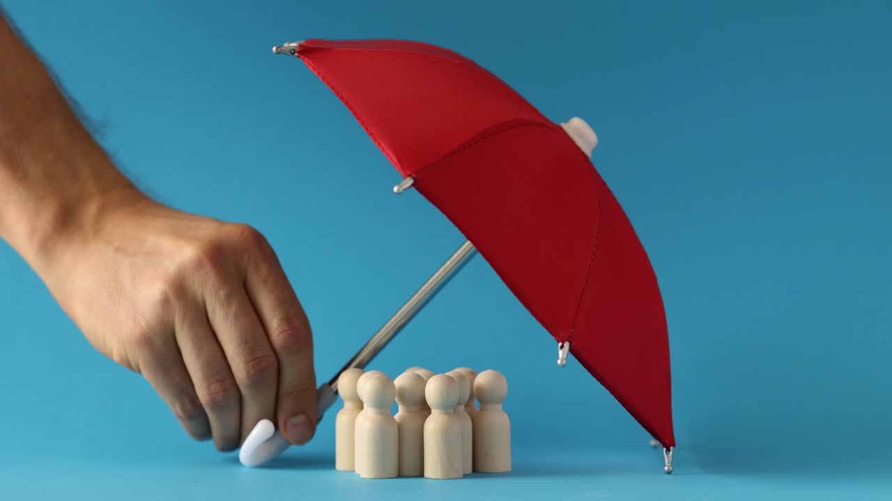 Hand Holding Red Umbrella Over Wooden Figures, Symbolizing Protection and Coverage