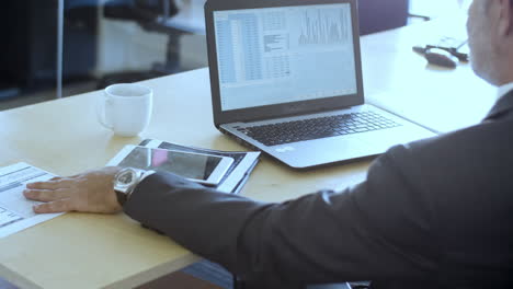 Mature-finance-professional-using-laptop-and-tablet-for-work