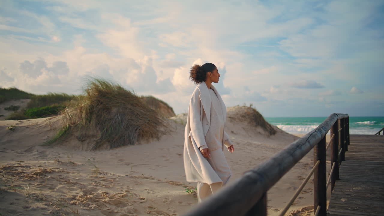 одинокая женщина гуляет по песчаному берегу во время весенних каникул. кудрявый путешественник восхищается океаном.