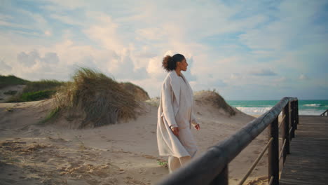 single woman walk sand shore on spring vacation. curly traveler admire ocean