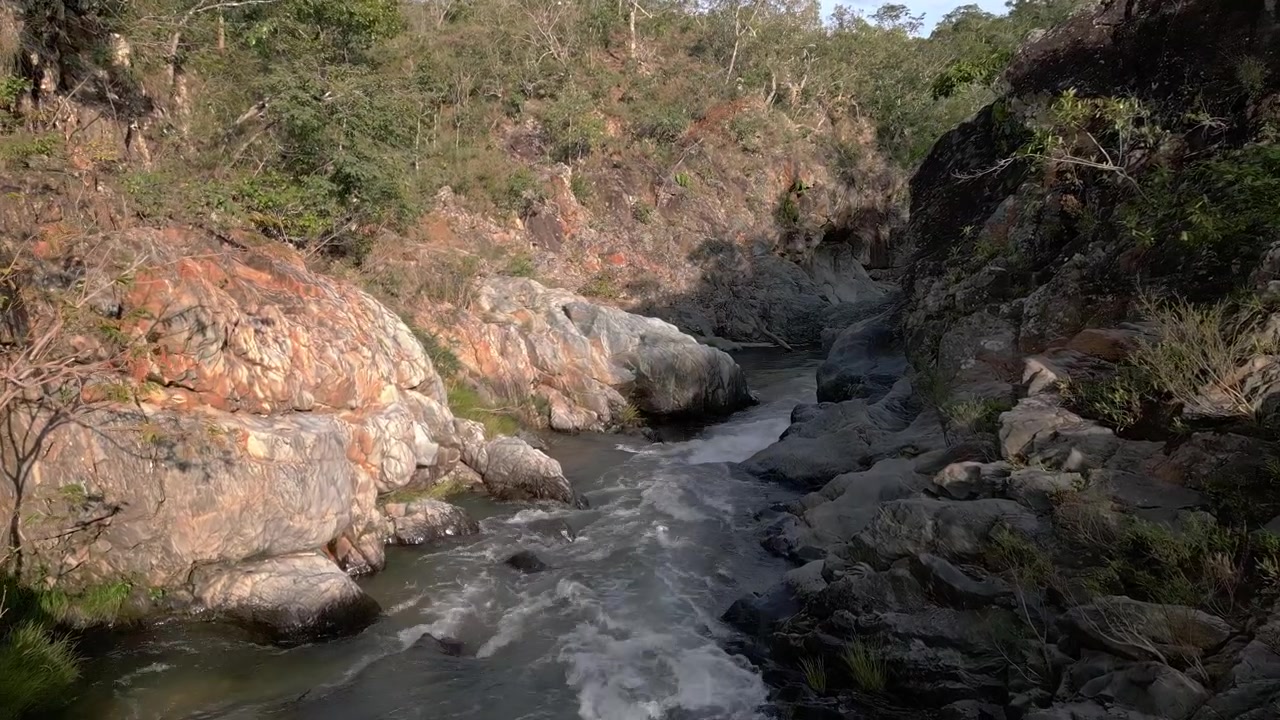 Il fiume São Miguel scorre attraverso un canyon di quarzite nella Serra do Segredo, Chapada dos Veadeiros, Goiás, Brasile, con pareti rocciose erose e una fitta vegetazione del Cerrado, ripresa con discesa a bassa parallasse e spinta in avanti.