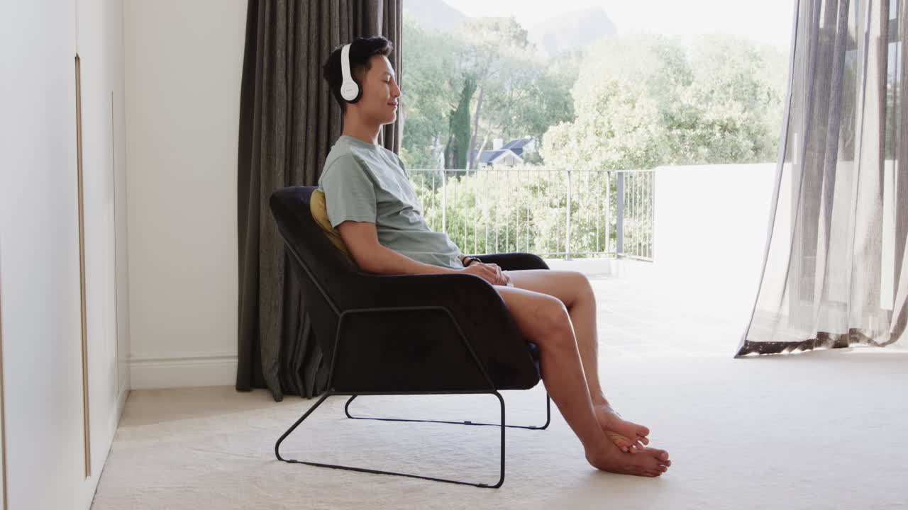 Relaxing at home, Asian man enjoying music with headphones, sitting peacefully