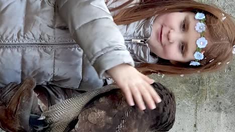 Smiling-little-girl-with-crown-of-flowers-caresses-tawny-owl-on-arm