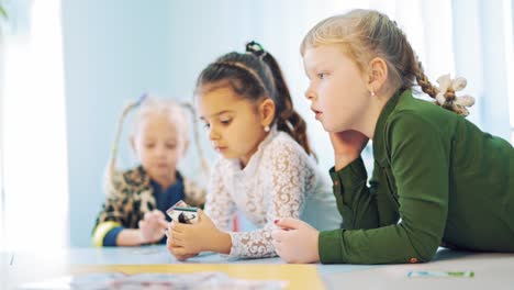 curious girls at the table at school. three mobile kids leaning on the table during the lesson. elementary school. close-up.