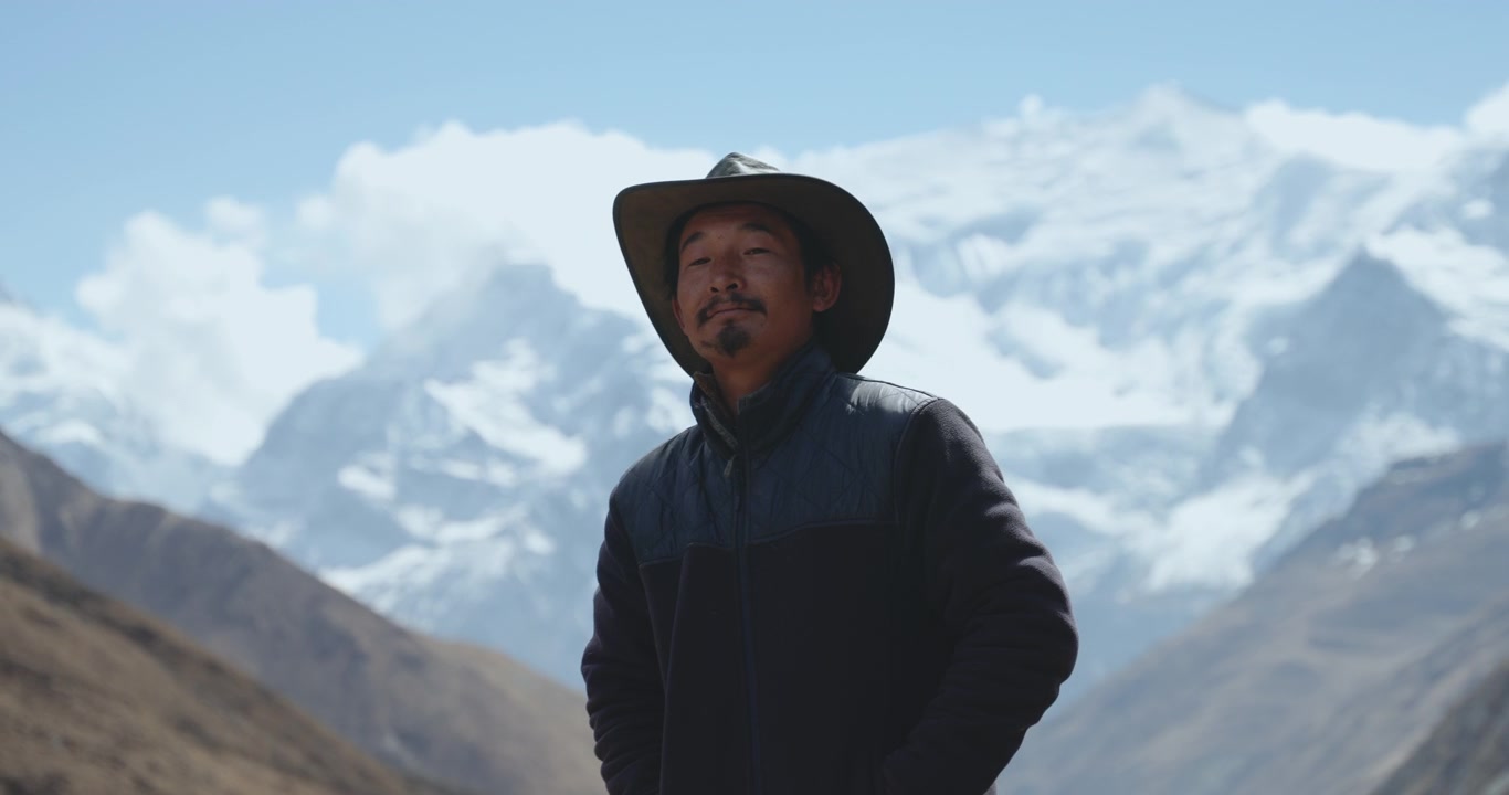 Circuito dell'Annapurna, Manang, Nepal, ripresa di un uomo Gurung locale che si sistema un cappello a tesa larga stile cowboy, sullo sfondo di cime dell'Annapurna morbide e sfocate
