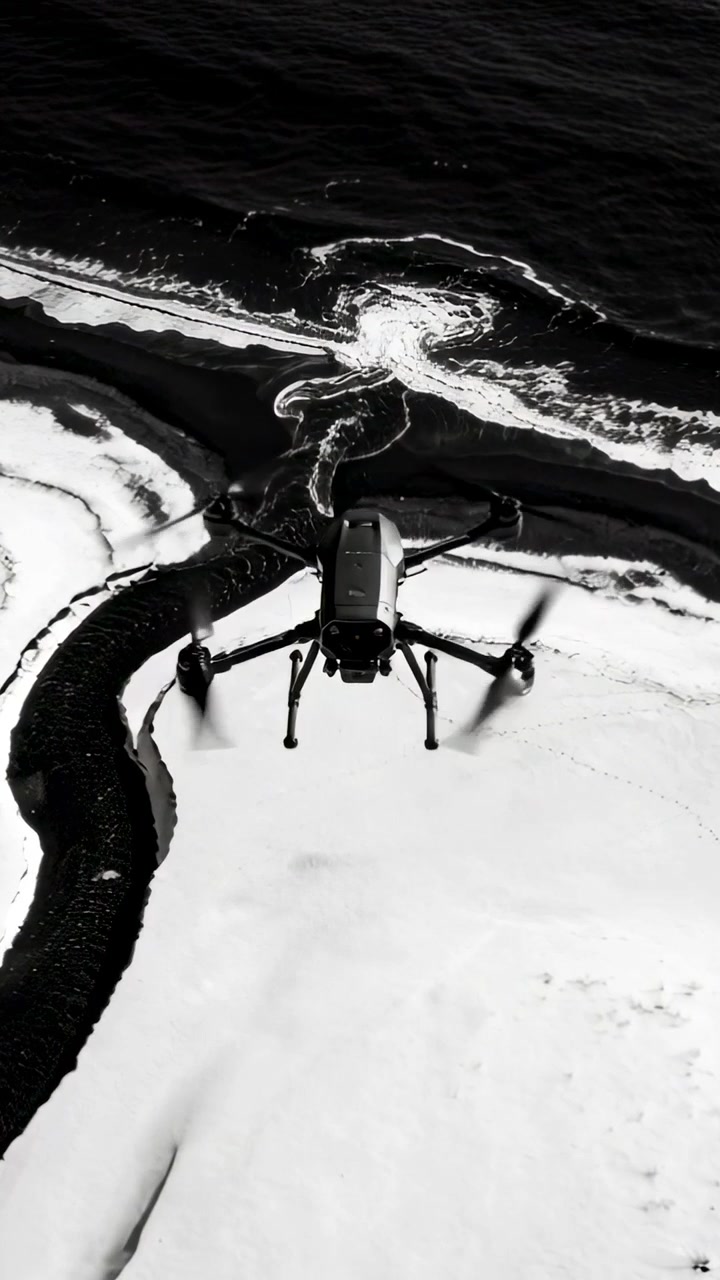 Vertical video: Rotors spinning, drone flying over black sand coast to surf, scanning tidal channel