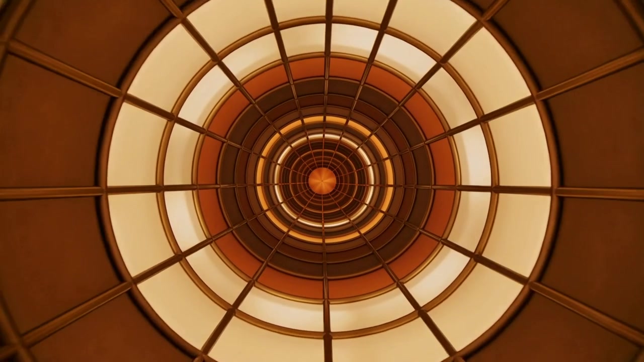 Telecamera che si avvicina muovendosi verso l'interno, verso una cupola circolare nell'atrio, mostrando un nucleo arancione, anelli illuminati e raggi di luce
