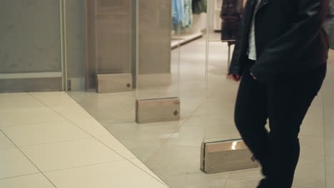 the lower part of people walking out of a clothing and shoe store is captured in this video. the video showcases the entrance of the store with clothing displays visible in the background