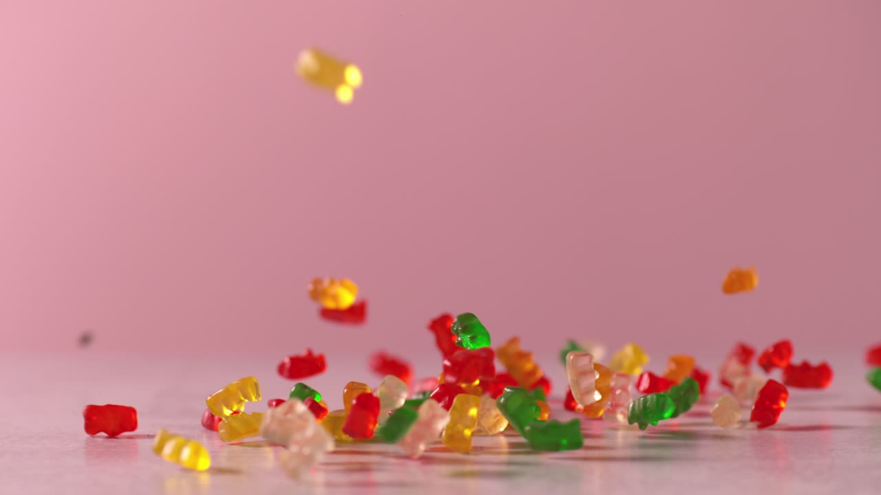 los osos de goma caen en cámara lenta sobre la superficie frente al fondo rosado