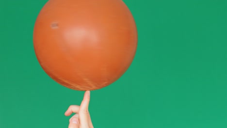 low angle view of a basketball ball spinning on a finger, green screen background, 4k slow motion