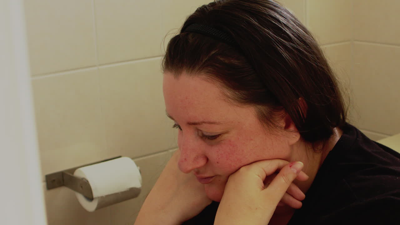 A shot of stress, in pain and a sad adult woman sitting in the toilet