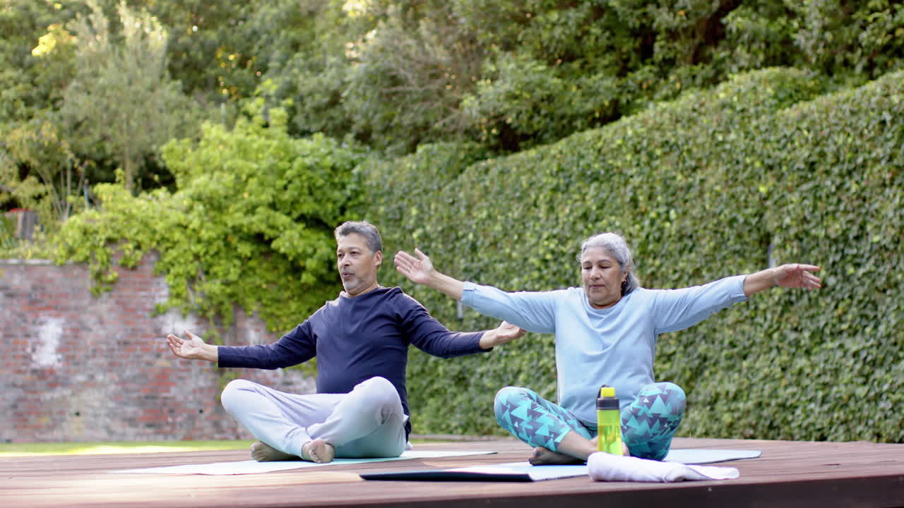 Coppia anziana multietnica concentrata che pratica yoga e meditazione in giardino.