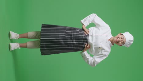 full body of asian woman chef with arms akimbo looking at camera and smiling while standing in the green screen background studio