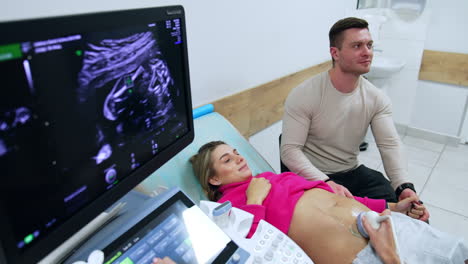 man and woman are in the doctor's cabinet. future parents are looking at ultrasound image of their future child.