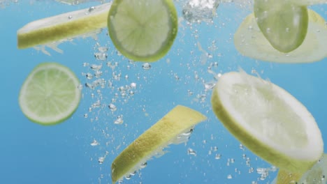 Video-of-slices-of-lime-and-lemon-falling-into-water-with-copy-space-on-blue-background