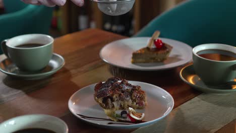 Cafe-table-with-coffee-cups-and-plate-with-dessert-pieces-while-the-pastry-chef-sprinkles-refined-sugar