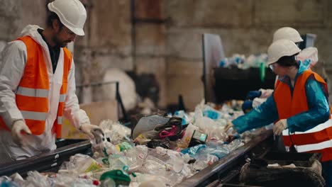 un hombre con un uniforme blanco un chaleco naranja y un casco blanco junto con dos de sus colegas clasifica botellas de plástico cerca de una cinta transportadora en una gran planta de reciclaje y clasificación de residuos