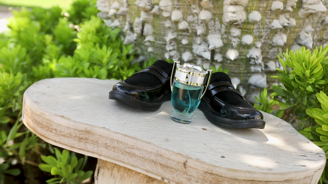 The shooting of the groom's black shoes and his perfume on the table in the garden for his wedding - pan left