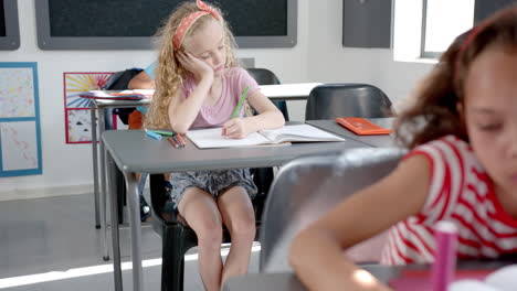 caucasian girl with blonde hair is deep in thought while writing in a classroom at school