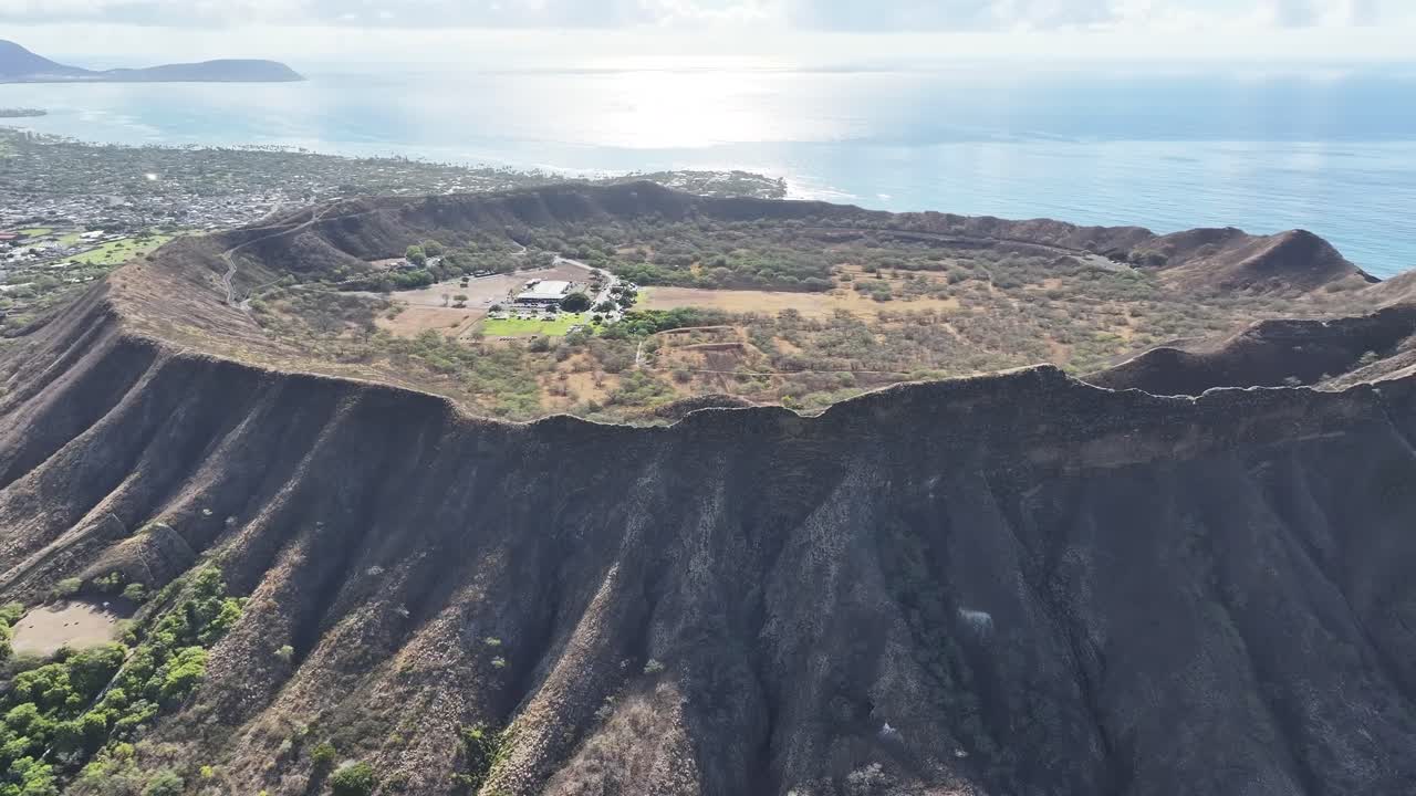 Aerial drone footage along the rim of Diamond Head volcanic crater on Oahu, Hawaii, showcasing panoramic tropical landscapes, turquoise ocean views, palm trees, and the scenic Waikiki coastline below