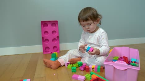 little baby girl playing with colorful plastic blocks on a floor