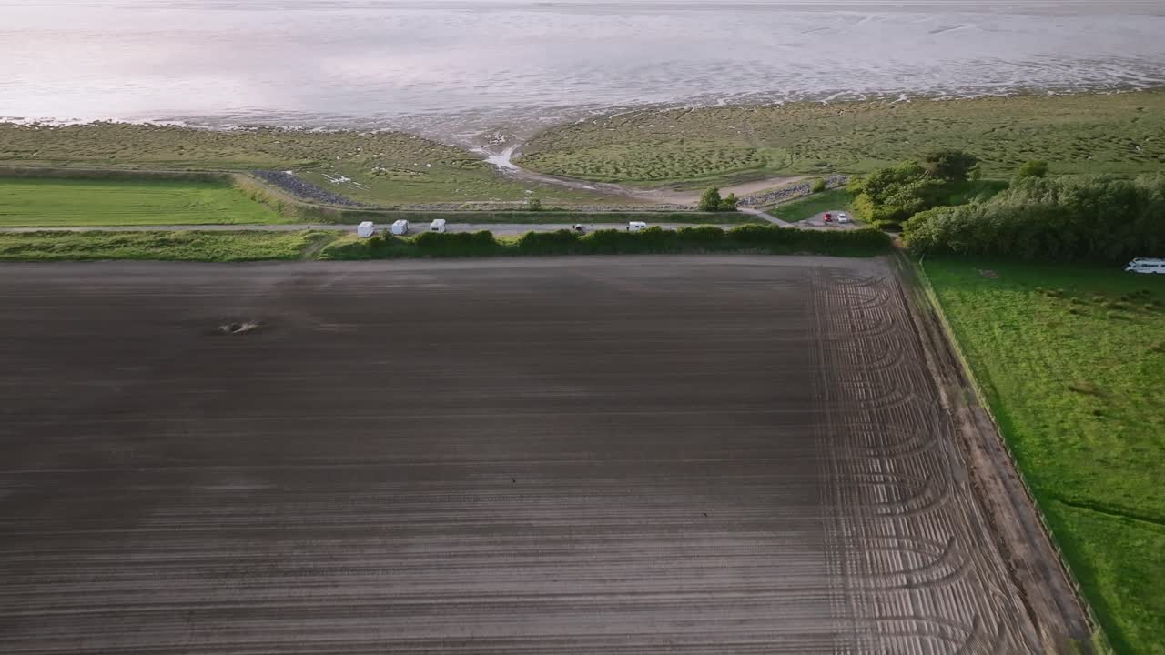 Flying over ploughed empty field towards coastline and tidal sands. Pilling Sands, Lancashire, UK.