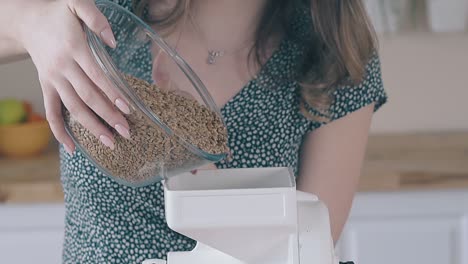 woman fills home flour grinder with raw wheat in kitchen