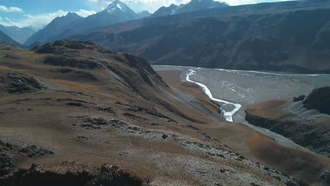 Autumn-aerial-of-a-high-altitude-rocky-mountain-range-with-river-stream-below