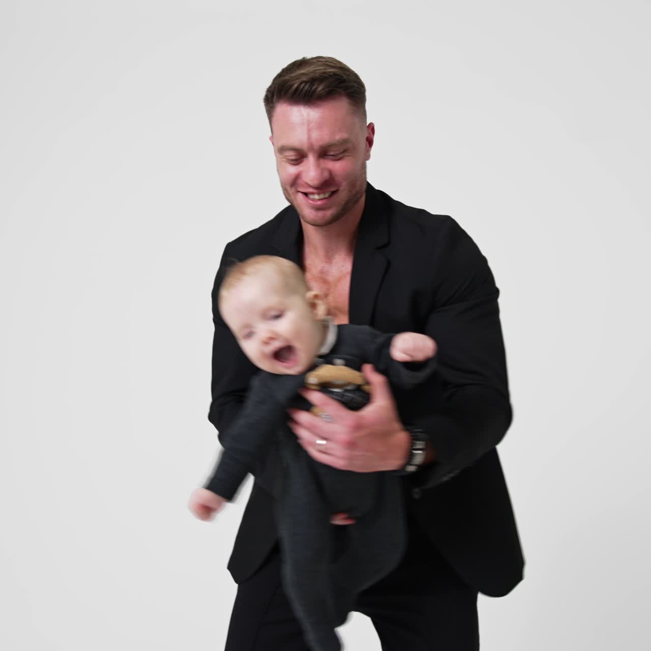 Glad, leende kaukasisk pappa som vinkar till sitt spädbarn. Man i svart kostym leker med sin underbara son. Vit bakgrund