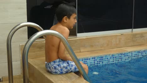 a small young boy sitting wet outside a swimming pool shivering from the cold one feels after getting out of the water