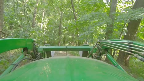 pov of equipment operator driving a loader with forks driving on a trail thru the woods on a sunny day in illinois