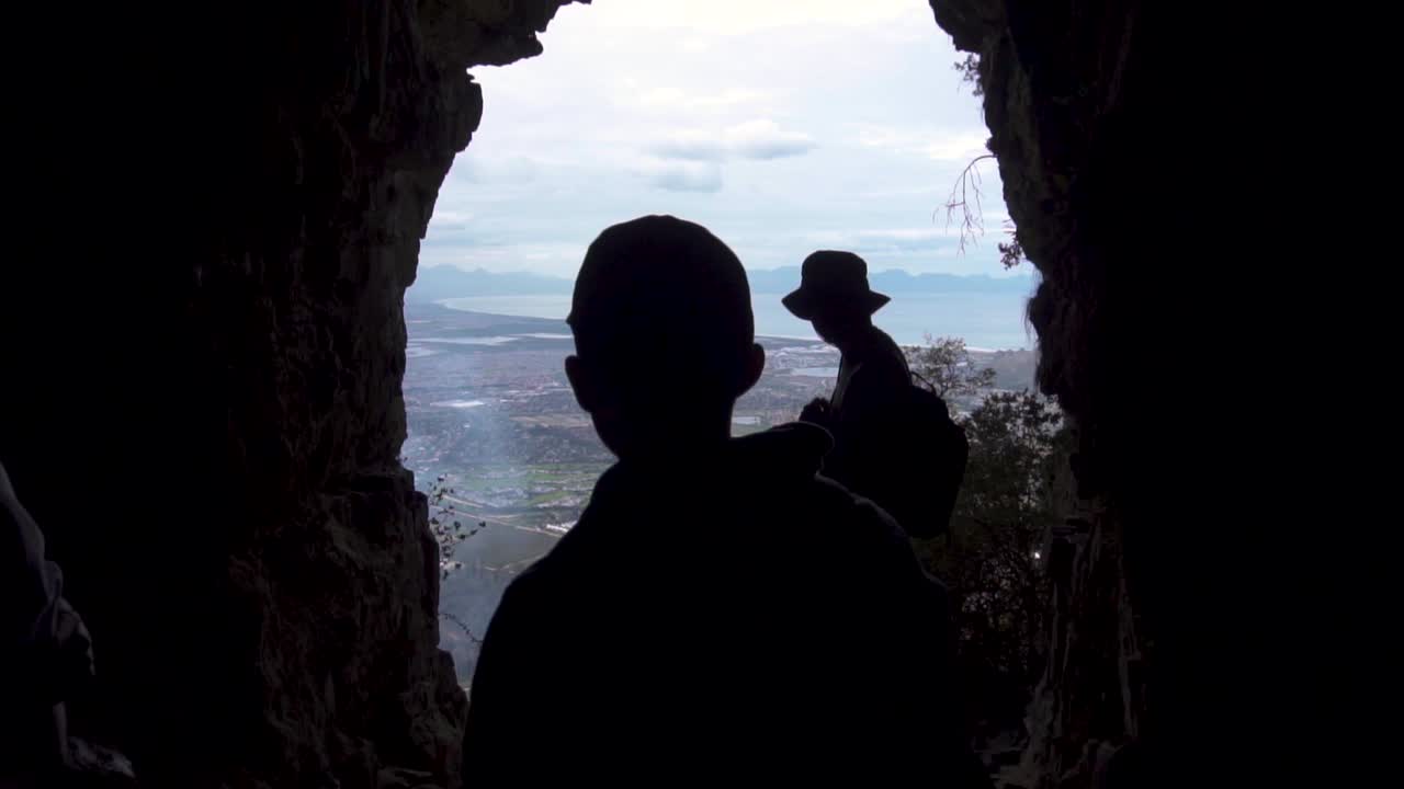 Hikers silhouetted in a cave overlooking a coastal city