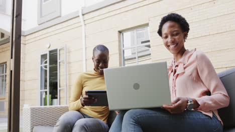 Two happy african american businesswomen talking, using technology outdoors, in slow motion